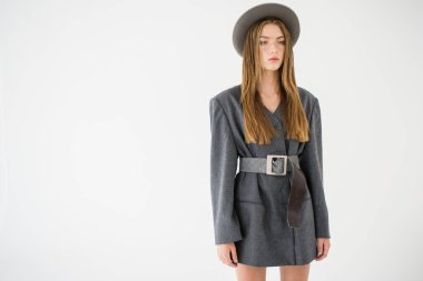 Çekici bir genç kız, gri ceketli bir manken ve elinde bir şapka tutuyor. Erkek tarzı kıyafetler. Beyaz bir arka planda izole edilmiş. Kenarında bir yazı için bir yer var. Seçici odak