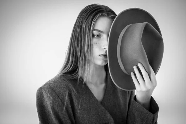 Portrait of an attractive young model looking to the side in a gray jacket and holding a hat in her hands. Men\'s style clothing. isolated on a white background. Selective focus. black and white