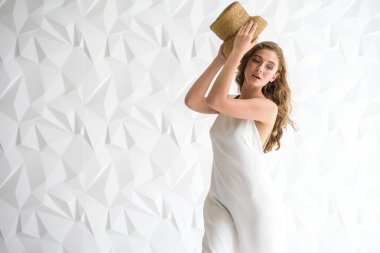 Aydınlık bir odada, açık renk bir elbise giymiş, hasır şapkalı genç bir kız. Seçici odak