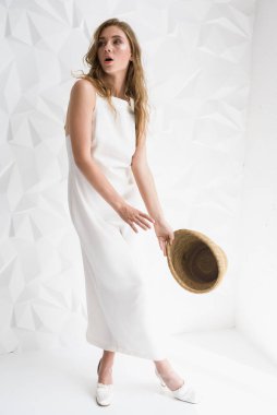 Aydınlık bir odada, açık renk bir elbise giymiş, hasır şapkalı genç bir kız. Seçici odak