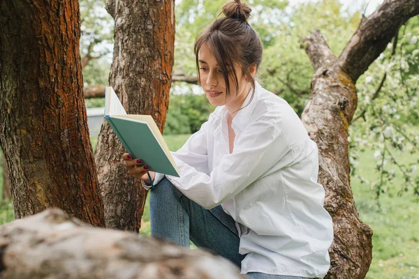 Self-isolation. Quarantine concept. Virus. morning, a young girl in a white shirt and blue jeans sitting in nature, on an apple tree, reading a book