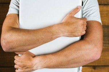 Genç adam önünde beyaz bir dizüstü bilgisayar tutuyor. Ahşap bir arka planda. Coronavirus kontrol konsepti. Uzaktan karantina