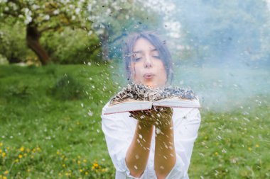 Açık tişörtlü kız elinde yanan bir kitap tutuyor. Elinde yanan bir kitap. Ormanda bir kitap yanıyordu. Ormanda genç bir kadın bir kitap yakıyor.