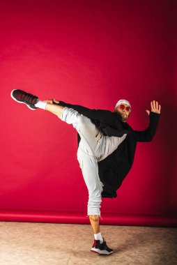 Uzun boylu, hoş, komik, çılgın, duygusal, yakışıklı, beyaz tişörtlü, kırmızı arka planda izole edilmiş spor kıyafetleri giyen adam.