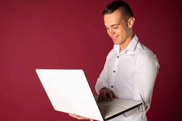 Confident business expert. Confident young handsome man in shirt holding laptop and smiling while standing on a red background