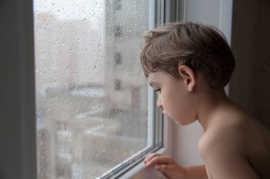 Küçük çocuk pencereden yağmuru izliyor. yakın plan