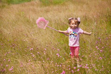 Küçük kız bir yaz çayırında kelebek ağı yakalıyor.