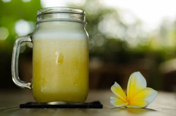 Frasco de vidro frio de suco tropical amarelo na mesa — Fotografia de Stock