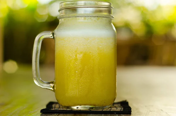 Frasco de vidro frio de suco tropical amarelo na mesa — Fotografia de Stock