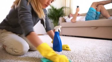 Kocası ile telefon kanepede yatıyor iken yorgun eşi halı temizler.