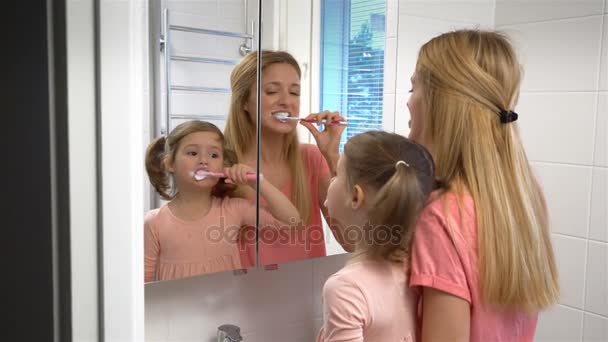 Joven atractiva mamá y su linda hija cepillarse los dientes . — Vídeos de Stock