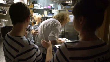 Küçük bir aile restoranı. Aşçı yemek hazırlar. Garsonlar vurgulu mutfakta