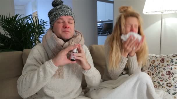 Krankes Paar mit laufenden Nasen benutzt Nasenspray und niest laut im Wohnzimmer.