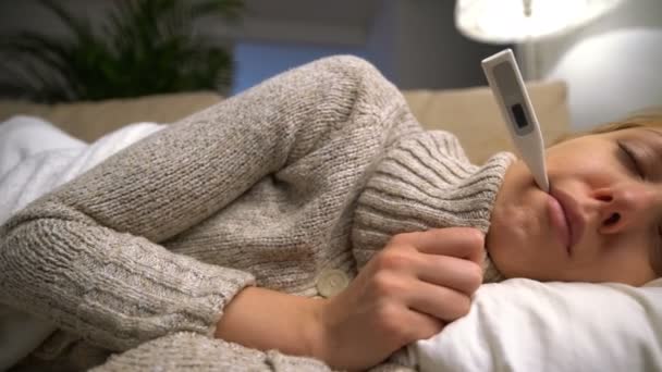Μια γυναίκα με πυρετό ξαπλωμένος στον καναπέ, με το θερμόμετρο στο στόμα του. Κουκλίτσα — Αρχείο Βίντεο
