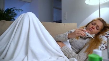 Ağzında bir termometre ile kanepede yatan ateş olan bir kadın. Dolly.