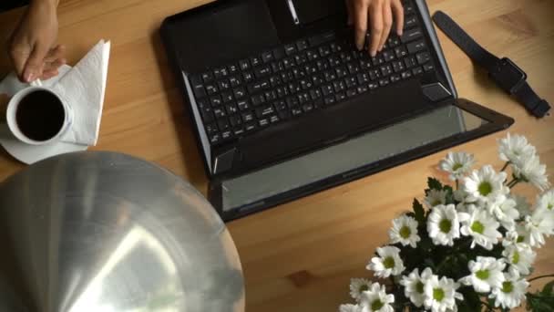 Жінка працює на комп'ютері з кавою та букетом квітів на столі . — стокове відео