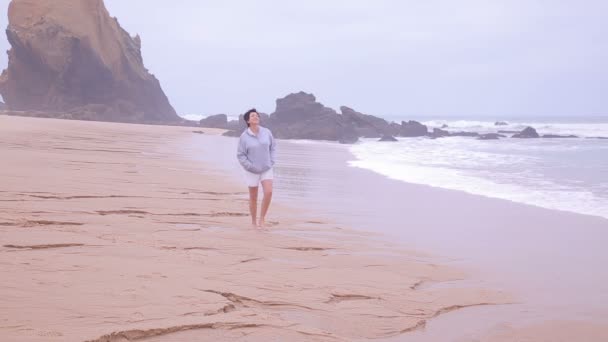 Attractive active senior woman walking along the ocean surf. — Stock Video