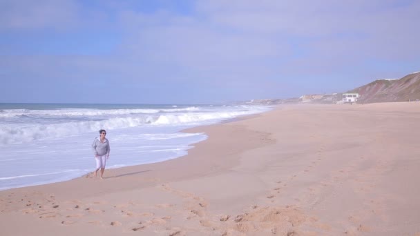 魅力的なアクティブ シニア女性は人けのない海ビーチの上を歩く. — ストック動画