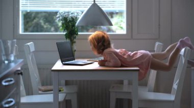 Küçük kız heyecanla masanın üzerinde yatan laptop çizgi film izlerken.