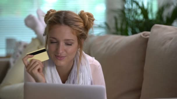 Mujer joven utiliza una tarjeta de crédito de oro en línea acostado en el sofá. Dolly Shot . — Vídeos de Stock