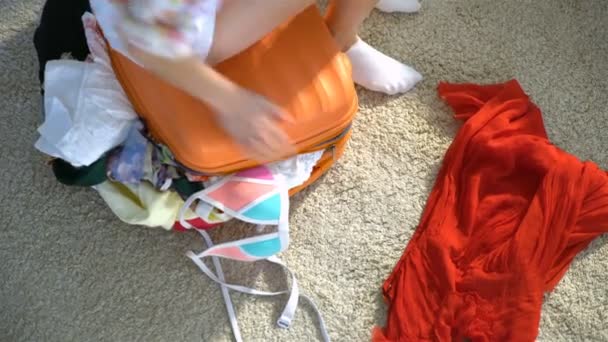 A young woman is trying to close a chock-full orange suitcase. Top view. — Stock Video