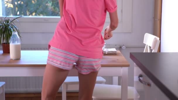 Een slanke gelukkige vrouw in pyjama voorbereiding van een gezond ontbijt en dansen. Slow motion — Stockvideo