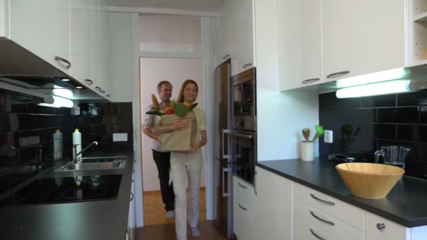 Το ευτυχισμένο ζευγάρι φέρνει στην κουζίνα μεγάλη σε χάρτινους σάκους των τροφίμων. Αργή κίνηση. — Αρχείο Βίντεο