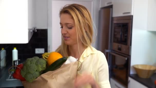 O femeie cu o pungă de alimente în bucătărie zâmbind la cameră. Slow Motion — Videoclip de stoc