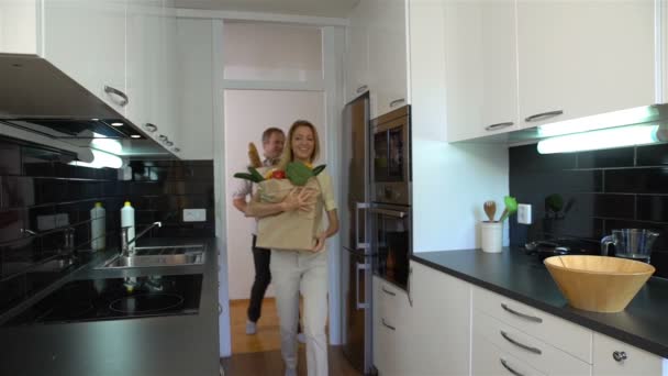 O casal feliz traz para a cozinha grandes sacos de papel de comida. Movimento lento . — Vídeo de Stock