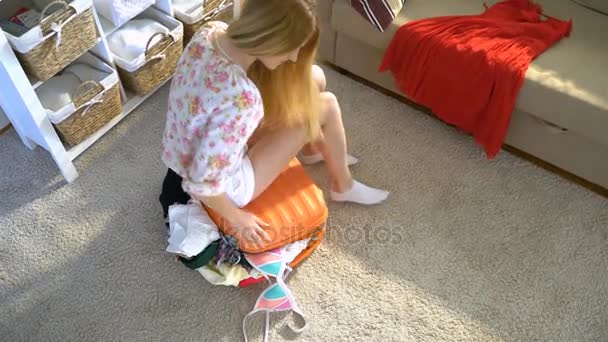 Молодая женщина пытается закрыть полный оранжевый чемодан. Вид сверху . — стоковое видео