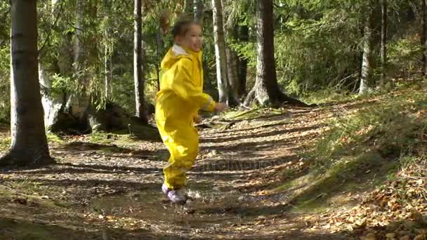Klein meisje in gele rubberen pak is in een plas springen. Slow Motion — Stockvideo