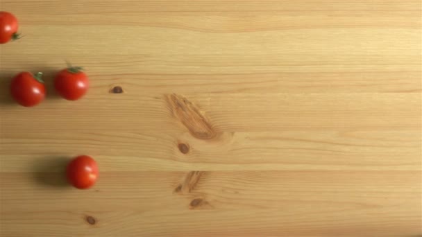 Beaucoup de tomates roulent sur la surface en bois. Au ralenti. Vue du dessus . — Video
