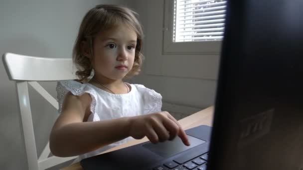 関心を持つ少女は、テーブルに座ってラップトップを使用しています。ドーリー ショット. — ストック動画