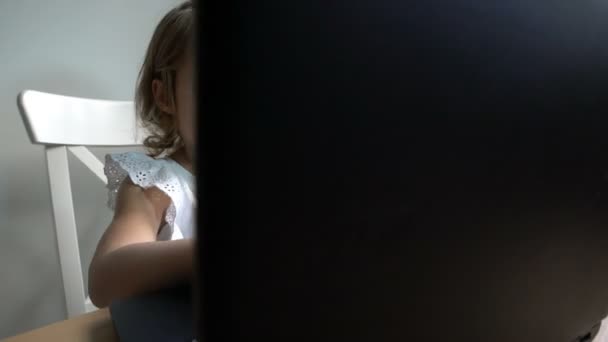 Little girl with interest uses the laptop sitting at the table. Dolly shot. — Stock Video