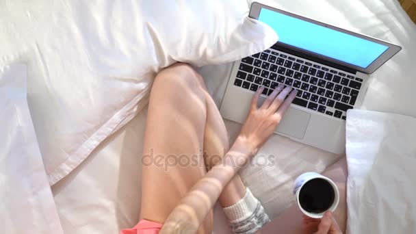 Γυναίκα σε pajama κάθεται στο κρεβάτι χρησιμοποιώντας φορητό υπολογιστή και να πίνει καφέ. Το Top view — Αρχείο Βίντεο