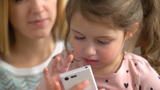 Genç anne ve kızı bir akıllı telefon çalmaya ve evde kanepede otururken gülümseyerek. Ağır çekim — Stok video