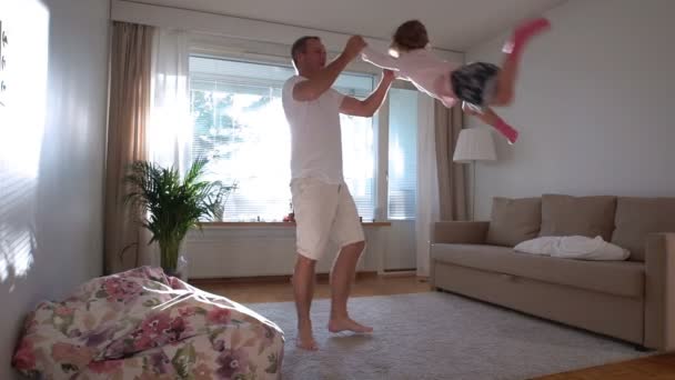 Pappa vänder och kastar upp lilla dotter på händer i soliga rummet. Slow motion — Stockvideo
