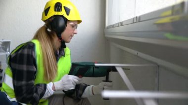 Beton duvar bir matkapla Delme ve kameraya gülümseyen genç kadın inşaat işçisi.