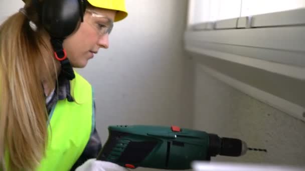 年轻女性的建筑工人用钻钻混凝土墙和对着镜头微笑. — 图库视频影像