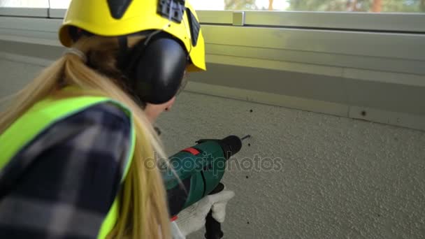 Junge Bauarbeiterin bohrt Betonwand mit Bohrmaschine an und lächelt in die Kamera. — Stockvideo