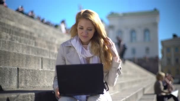 Young woman uses a laptop on the stairs in the center of the city — Stock Video