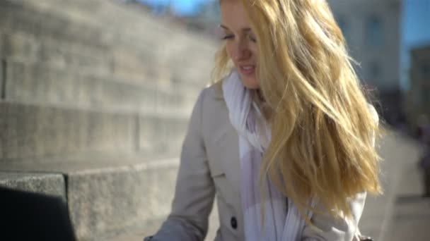 Mujer joven utiliza un ordenador portátil en las escaleras en el centro de la ciudad — Vídeo de stock