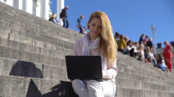 Young woman uses a laptop on the stairs in the center of the city — Stock Video