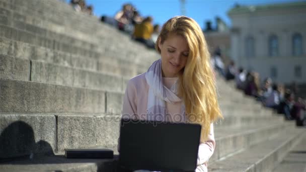 Mladá žena odkládá laptop a zvedne knihu na schodech v centru města — Stock video