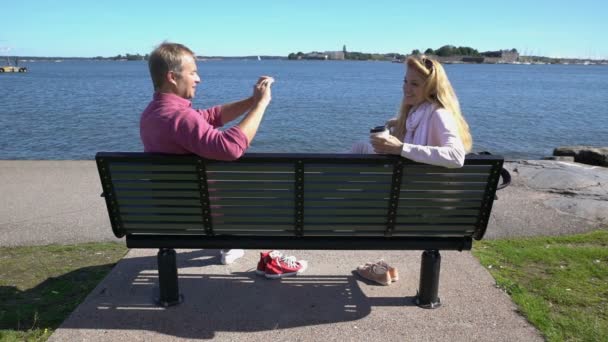 Un joven está fotografiando a su novia usando un teléfono inteligente junto al mar. Movimiento lento — Vídeo de stock