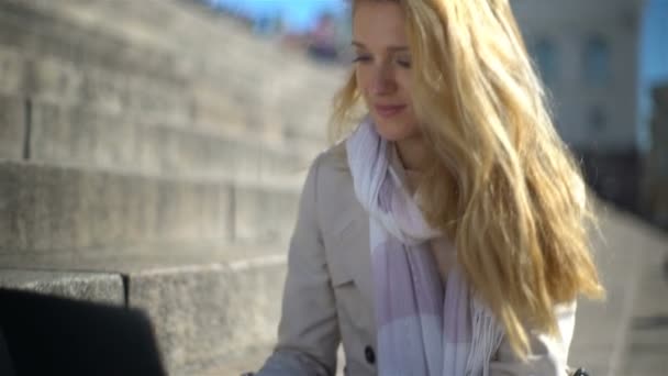 Young woman uses a laptop on the stairs in the center of the city. Slow motion — Stock Video