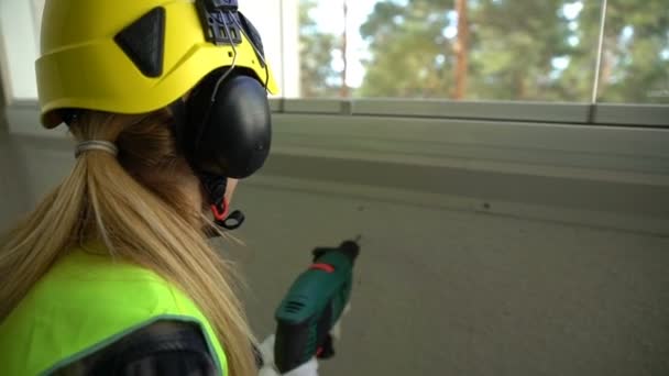 Jeune ouvrière de la construction forant un mur de béton avec une perceuse et souriant à la caméra . — Video