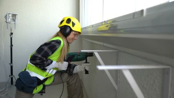 Jovem trabalhadora da construção civil perfurando parede de concreto com uma broca e sorrindo para a câmera . — Vídeo de Stock