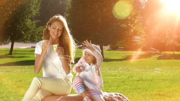 Junge Mutter und ihre Tochter spielen im Park mit Seifenblasen. — Stockvideo