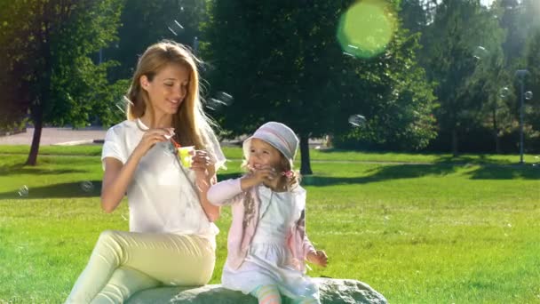 Junge Mutter und ihre Tochter spielen im Park mit Seifenblasen. — Stockvideo